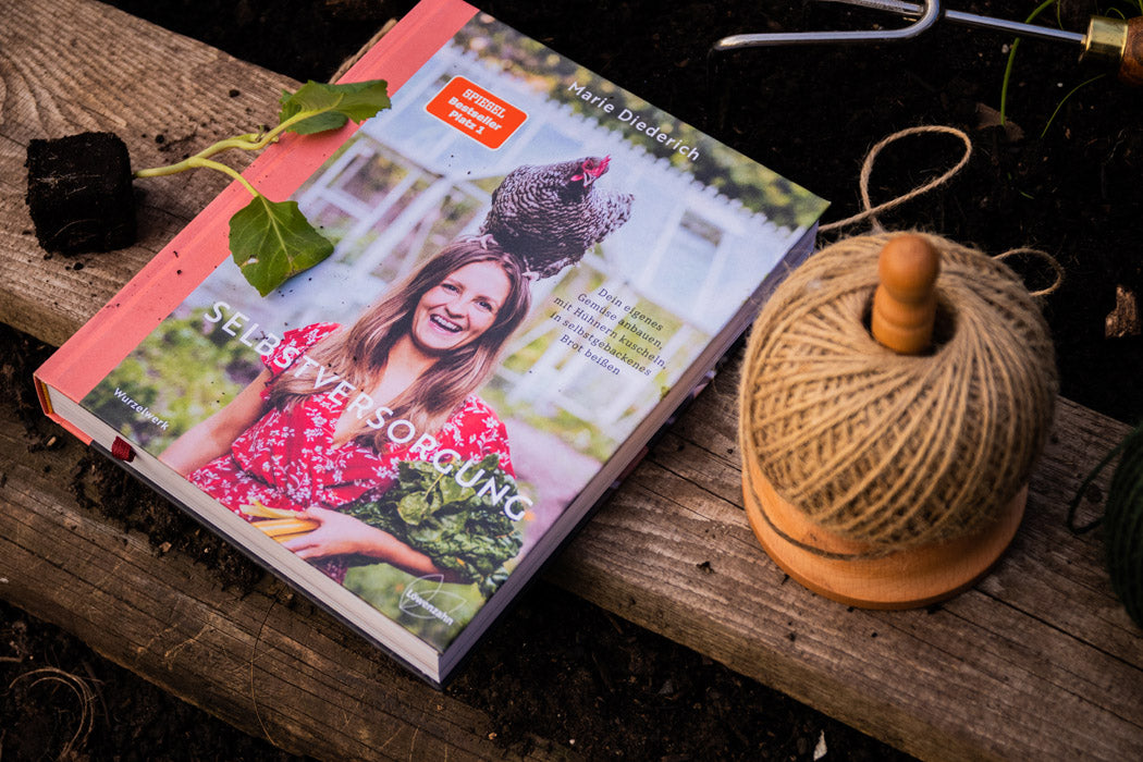 Buch "Selbstversorgung" auf dem Hochbeet mit Jungpflanze und Schnurr