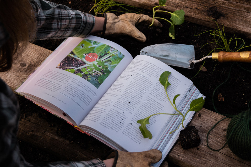 Buch "Selbstversorgung" auf einem Hochbeet, während der Bepflanzung